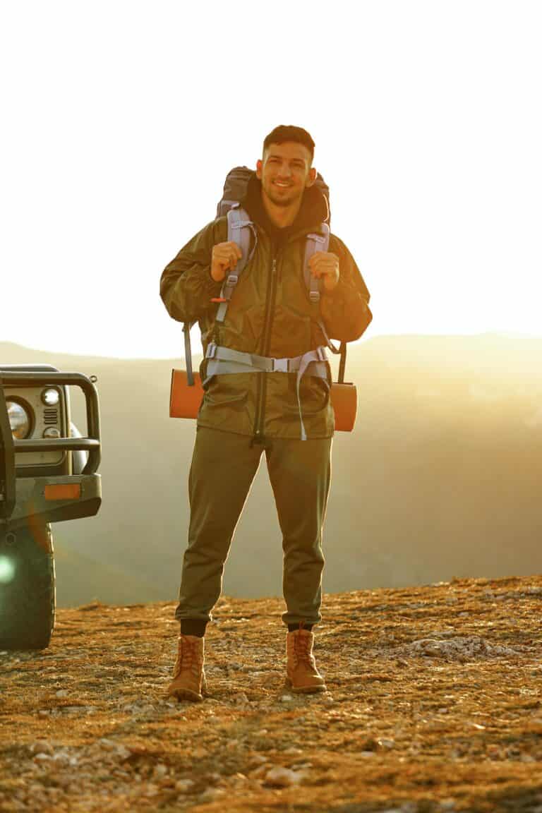 Portrait of a young traveler man in hiking equipment standing near his off-road car