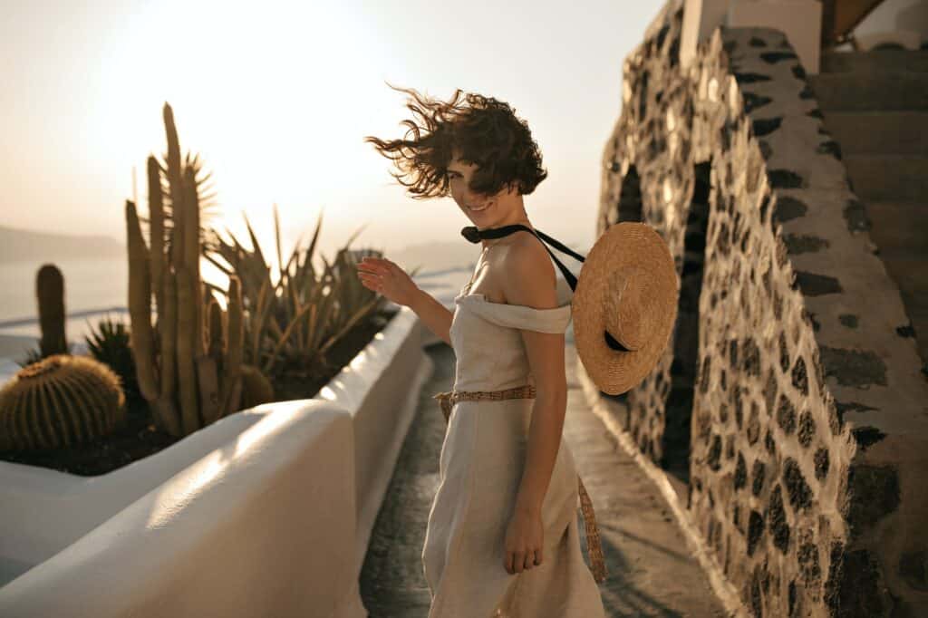 Portrait of charming curly brunette woman in beige dress and straw boater smiles and moves in beaut